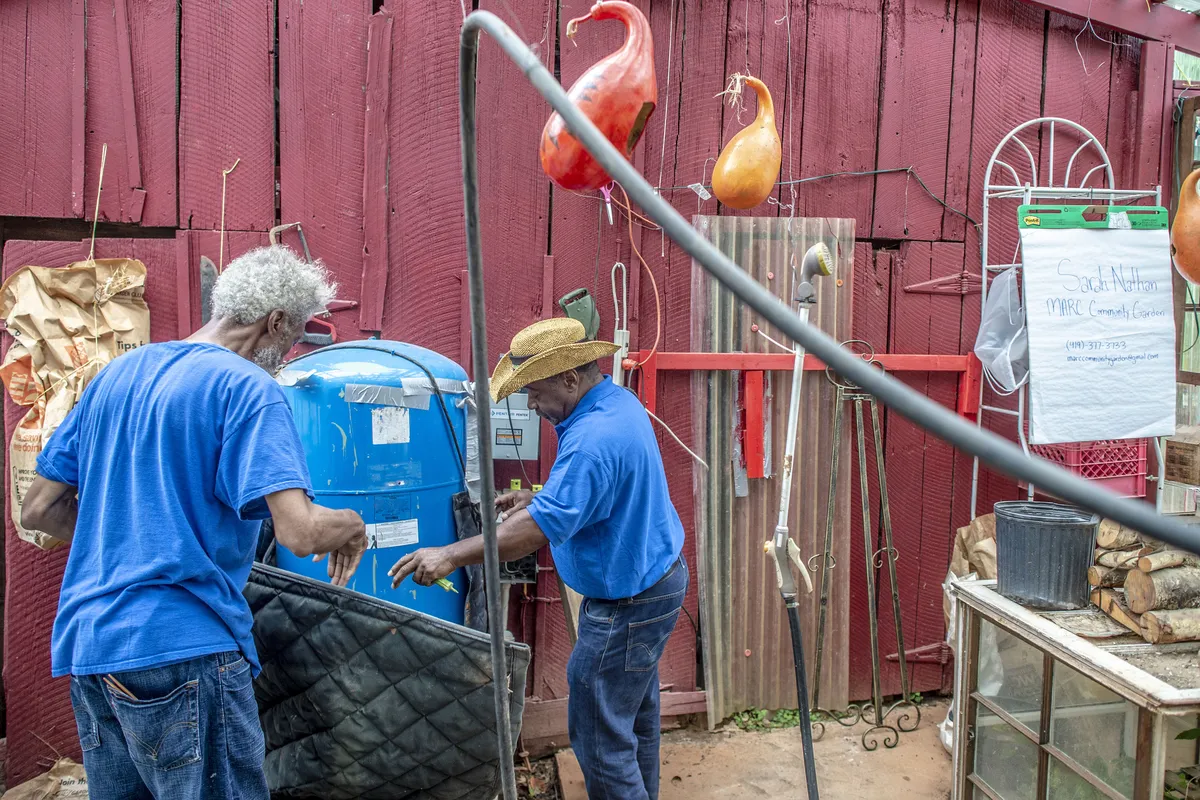 Two farmers working beside a blue tank at the farm shed