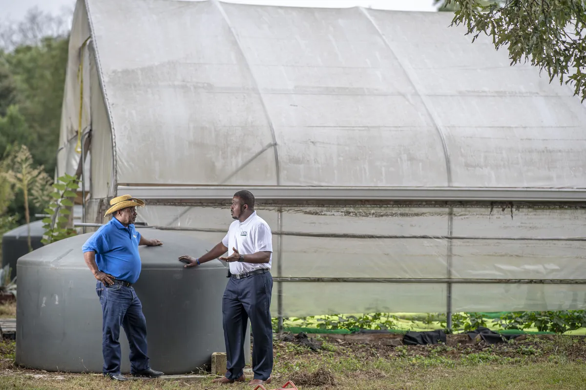Bobby Wilson talking with a visitor beside a water tank and hoop house