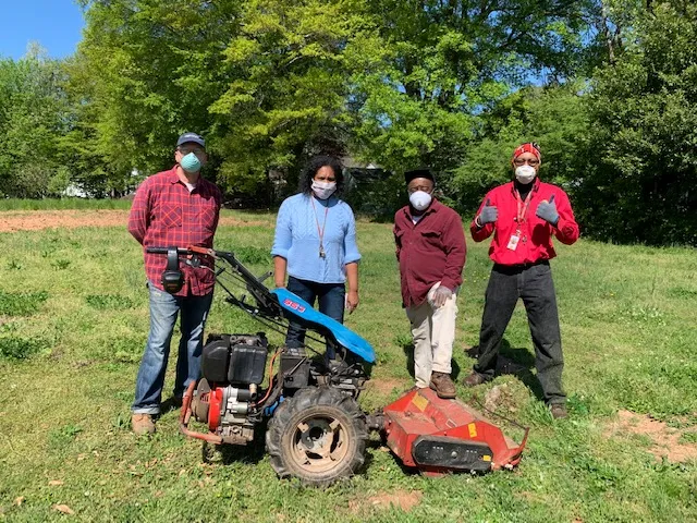 Four volunteers standing with a walk-behind tractor in a grassy field